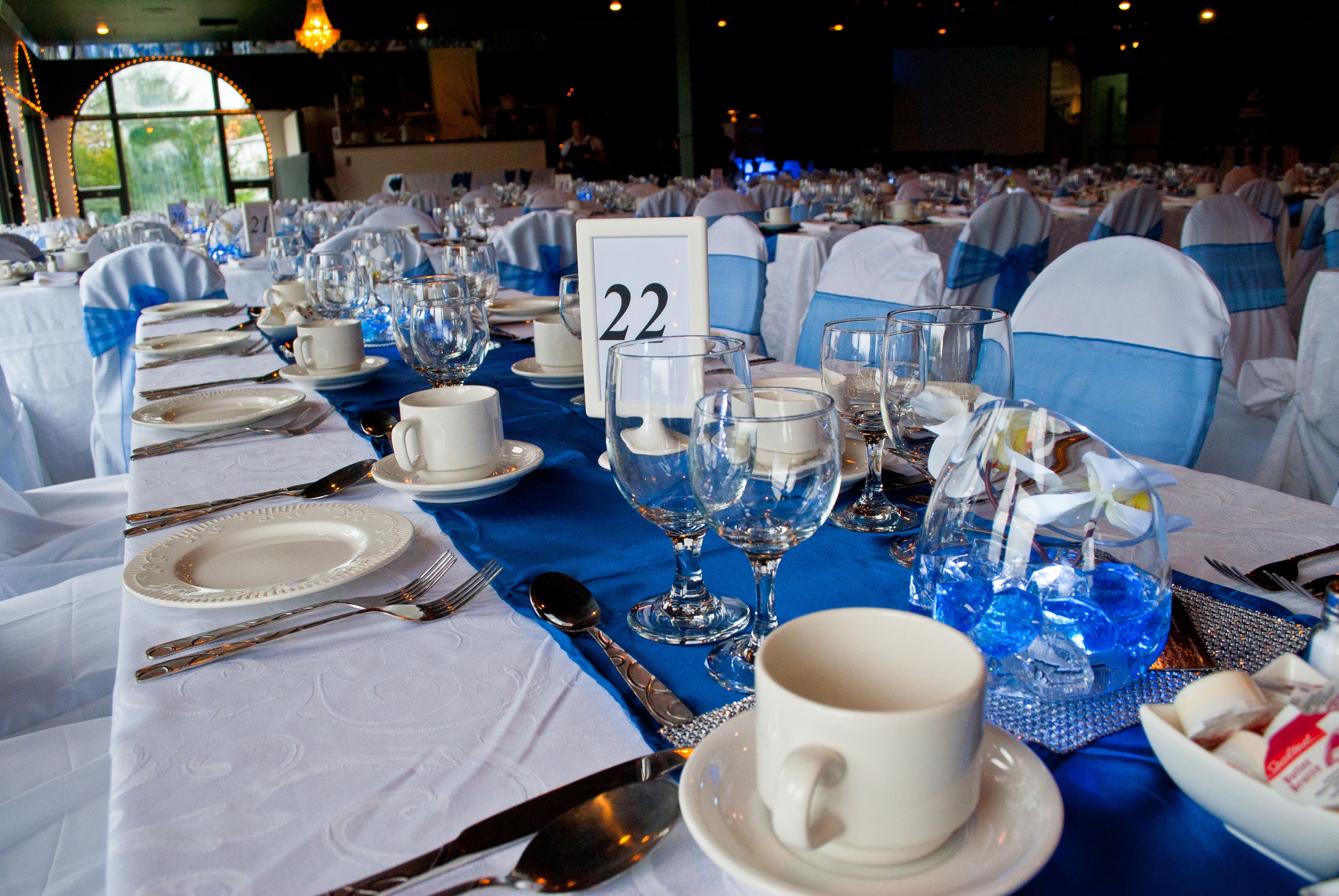 A banquet hall with tables set for a formal event, each with numbered place settings and blue sashes.