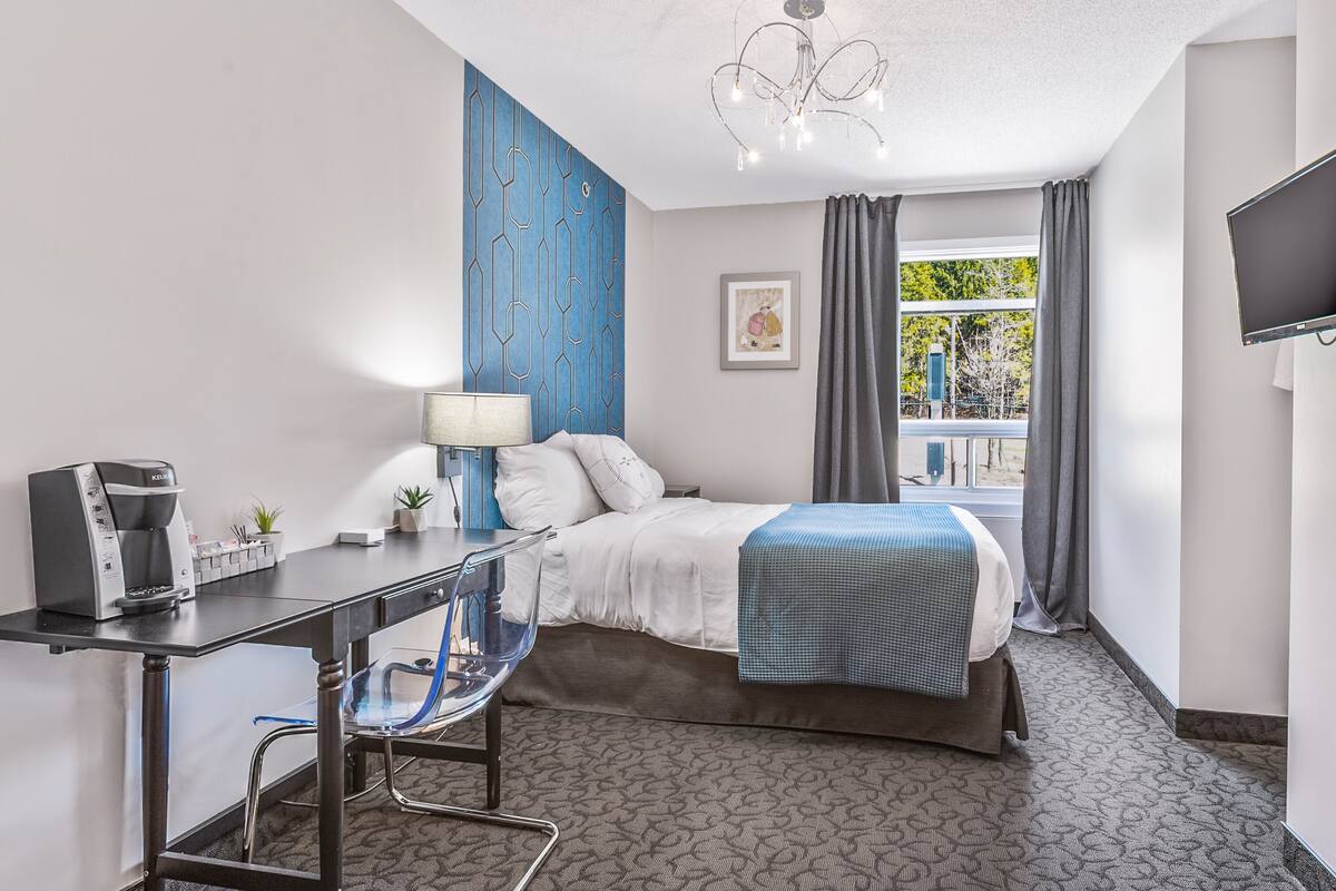 Habitación de hotel con cama, escritorio, silla, cafetera y televisor.