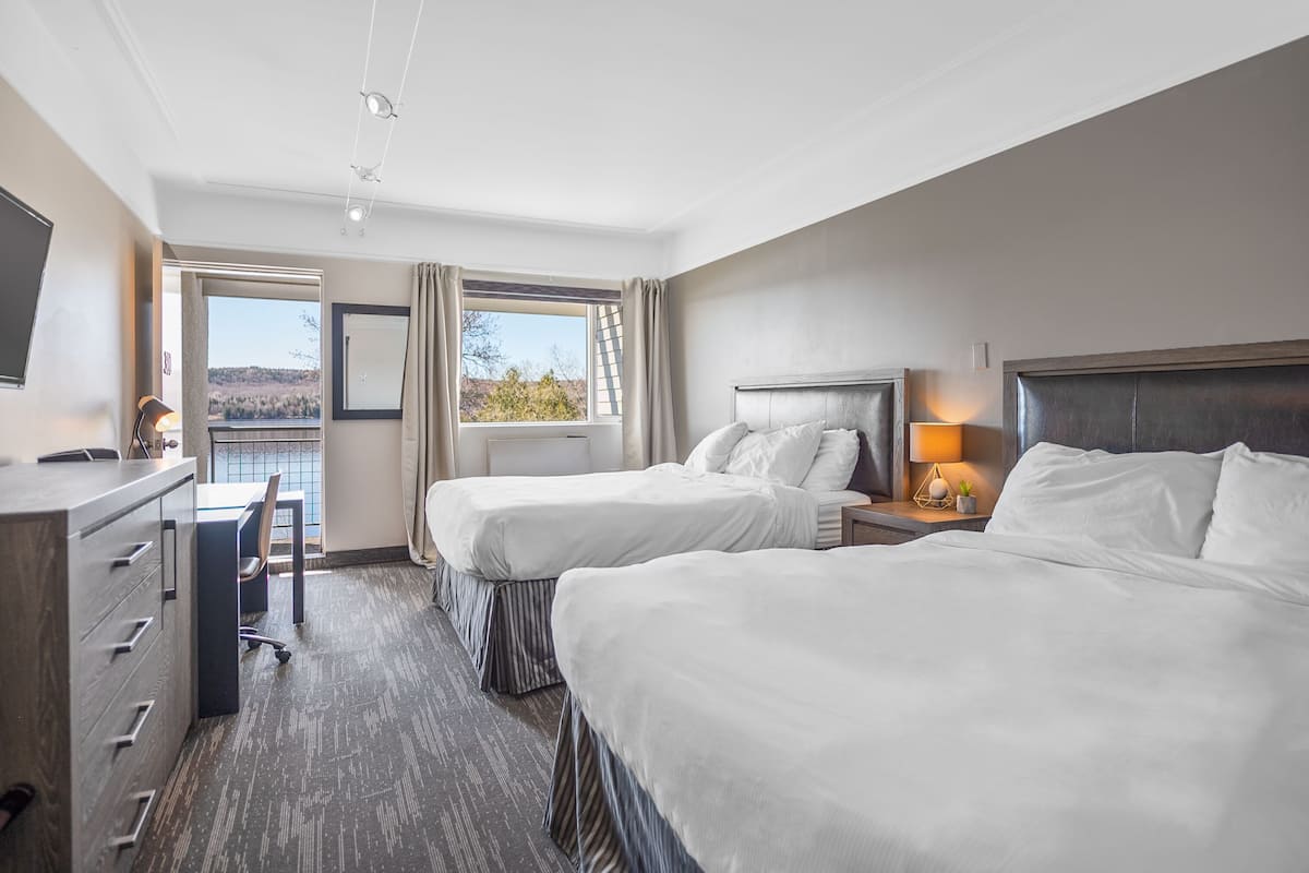 Habitación de hotel con dos camas, un escritorio y una silla. Se ve un ventanal con vistas al exterior.