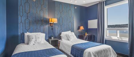 A hotel room with two beds, a chandelier, a window with a view, and patterned walls.