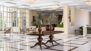 Un vestíbulo amplio con una mesa grande, candelabros elegantes y vistas al exterior a través de amplias ventanas.