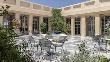 A courtyard with outdoor seating, a central fountain, and a tall tree.