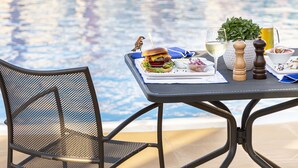 Mesa de comedor con una hamburguesa, ensalada y bebidas, con vistas a una piscina.