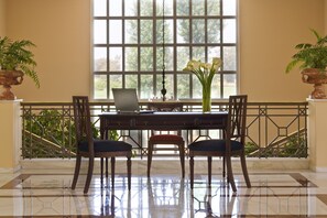 Una habitación con un ventanal grande, un escritorio con una computadora portátil, dos sillas y un florero con flores.