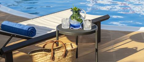 A poolside area with a lounge chair, a small table with a pitcher of water, two glasses, and a woven basket.