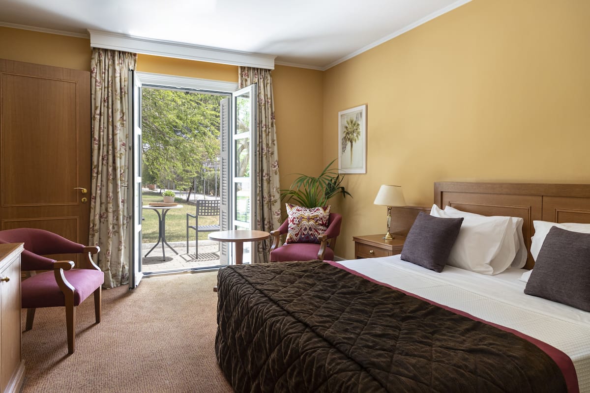 A hotel room with a bed, a desk, a chair, a small table, and a view of the outdoors.
