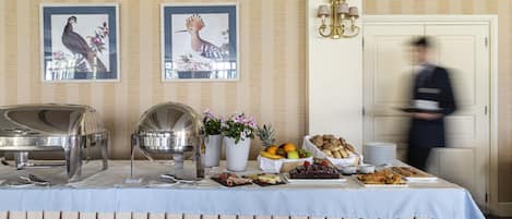 A buffet table with various food items, a potted plant, and two framed bird pictures on the wall.