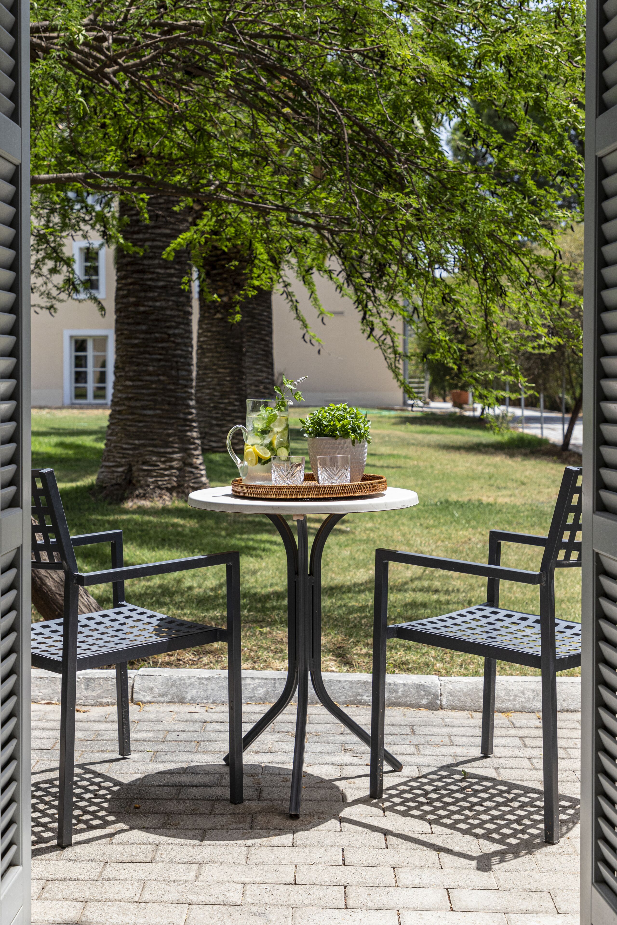 Un patio con una mesa redonda y dos sillas, una planta en maceta y una jarrón con agua.