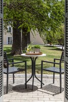 Un patio con una mesa redonda y dos sillas, una planta en maceta y una jarrón con agua.