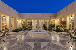 A courtyard with a central fountain, surrounded by seating areas and a building facade with large windows and doors. - Amalia Hotel Nafplio (Nafplio)