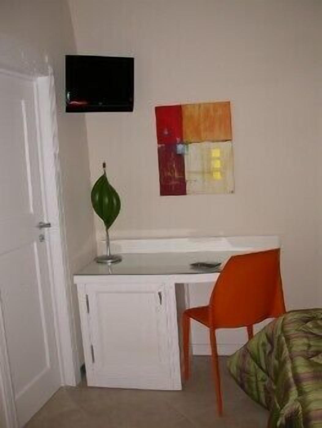 A small room with a white desk, an orange chair, a television mounted on the wall, and a green decorative item on the desk.