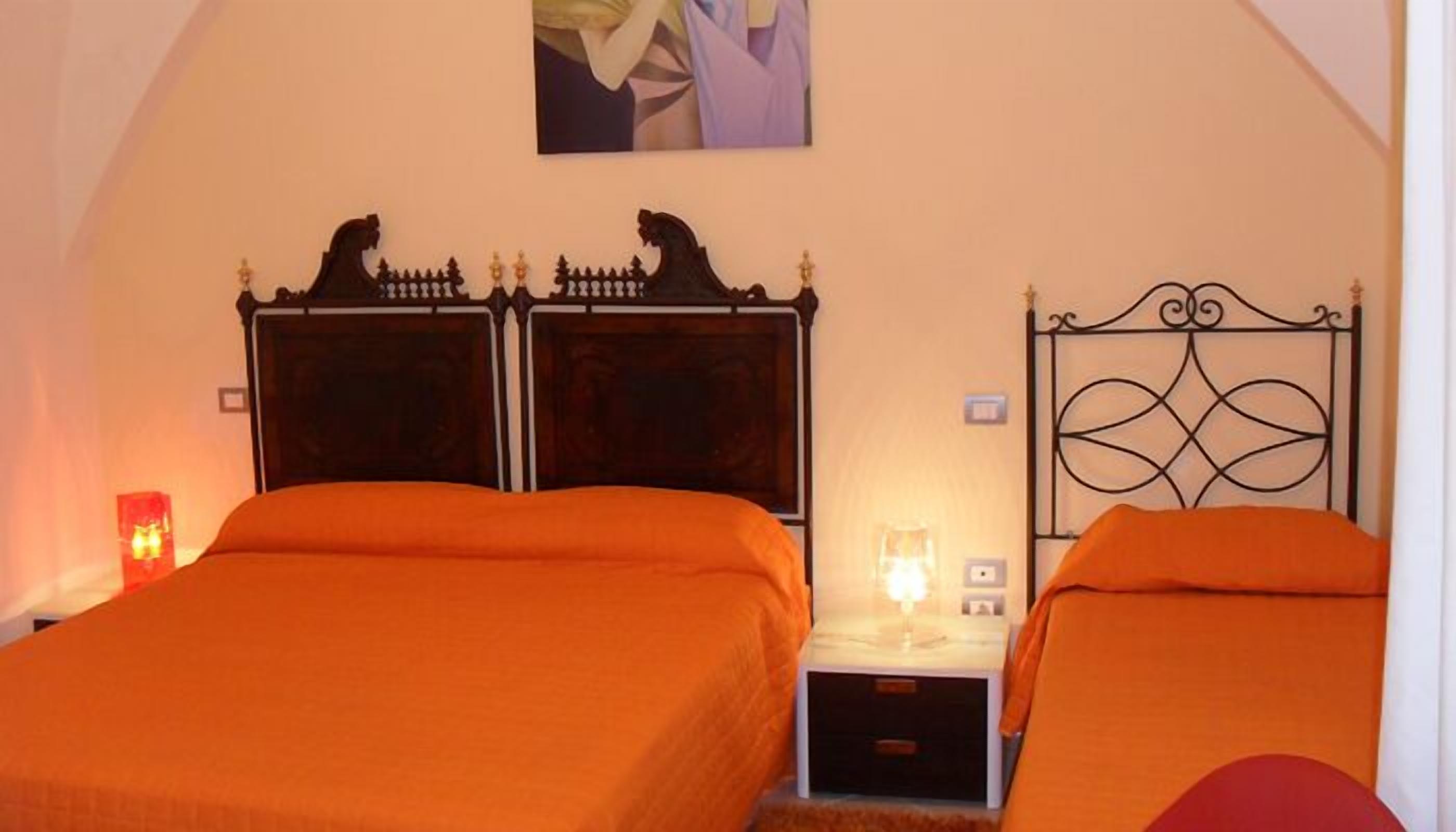 Quarto com duas camas, cada uma com cabeceira escura e roupa de cama laranja.
