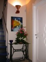 Un pasillo con una escalera, un cuadro, un florero con flores y una mesa.