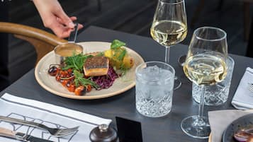 A dining table with a plate of food, two glasses of white wine, and a water glass.