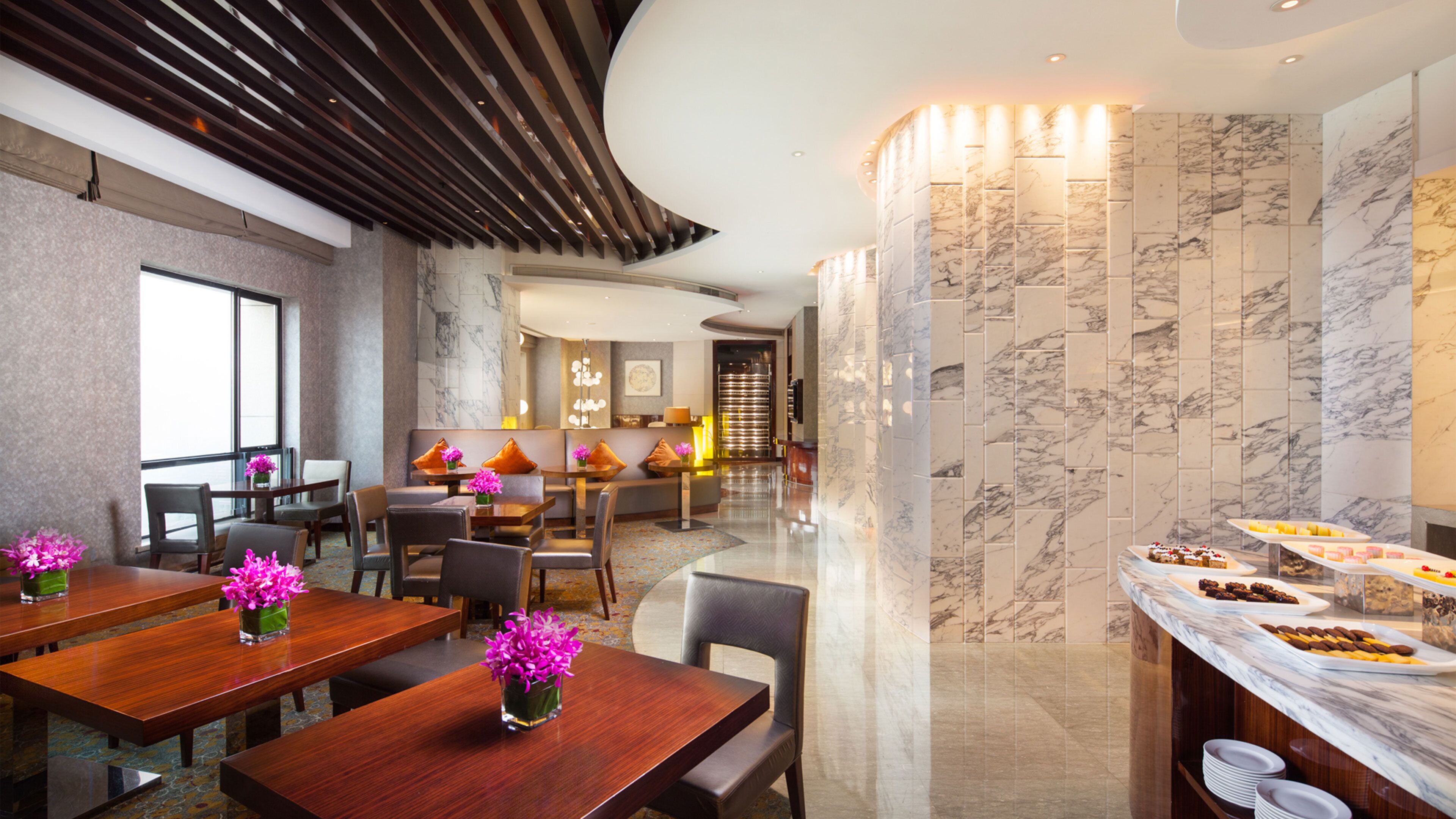 Une salle à manger d’hôtel avec des murs en marbre, des tables en bois et un buffet proposant une variété de plats.