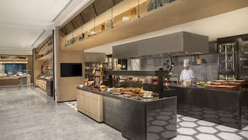 A modern kitchen with a central island, a chef at work, and a variety of food items displayed.