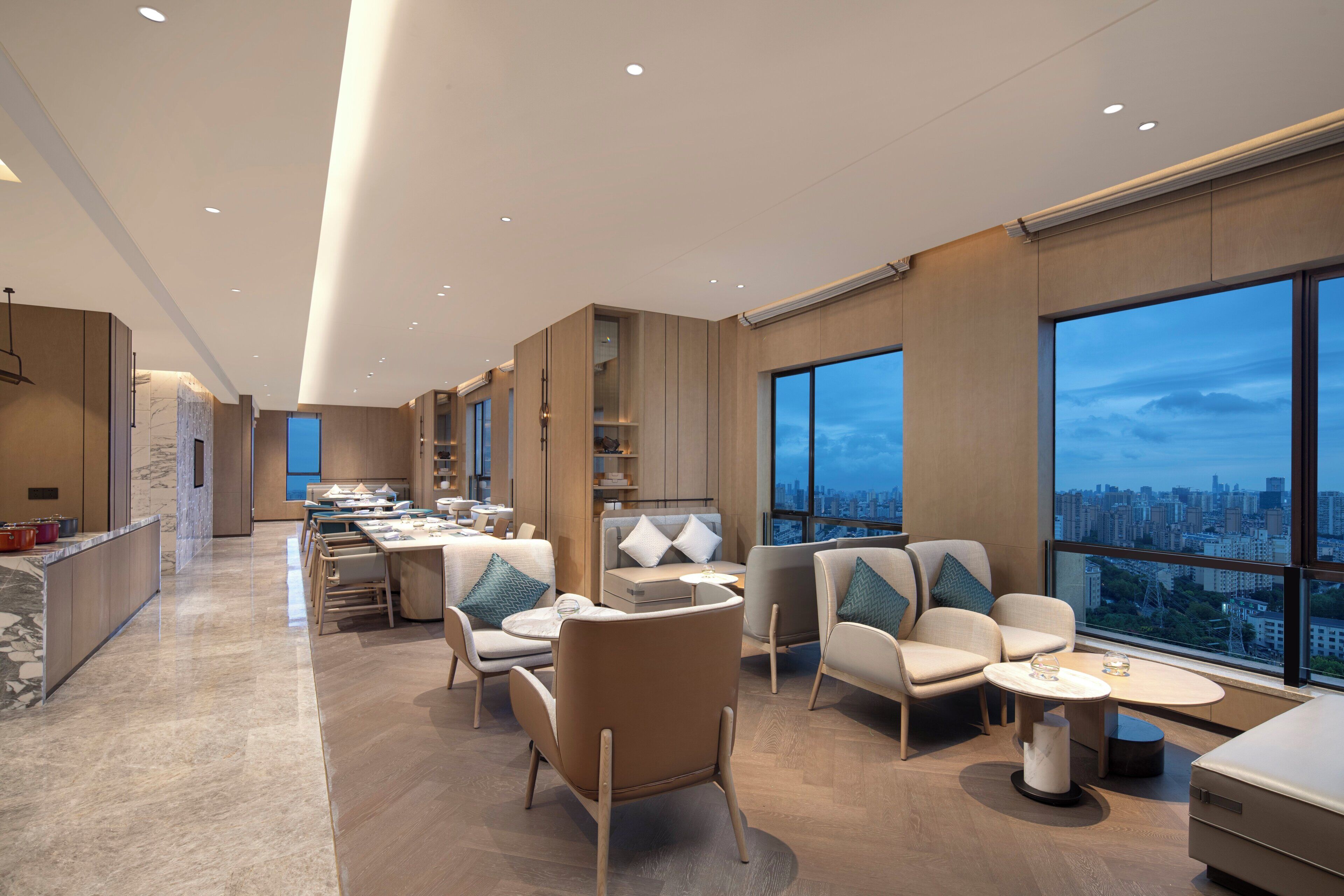 En moderne hotellobby med siddepladser, et tekøkken og store vinduer med udsigt over byen.
