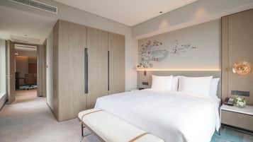 A modern hotel room with a large bed, a bench, a desk with a phone, and a wall-mounted artwork.