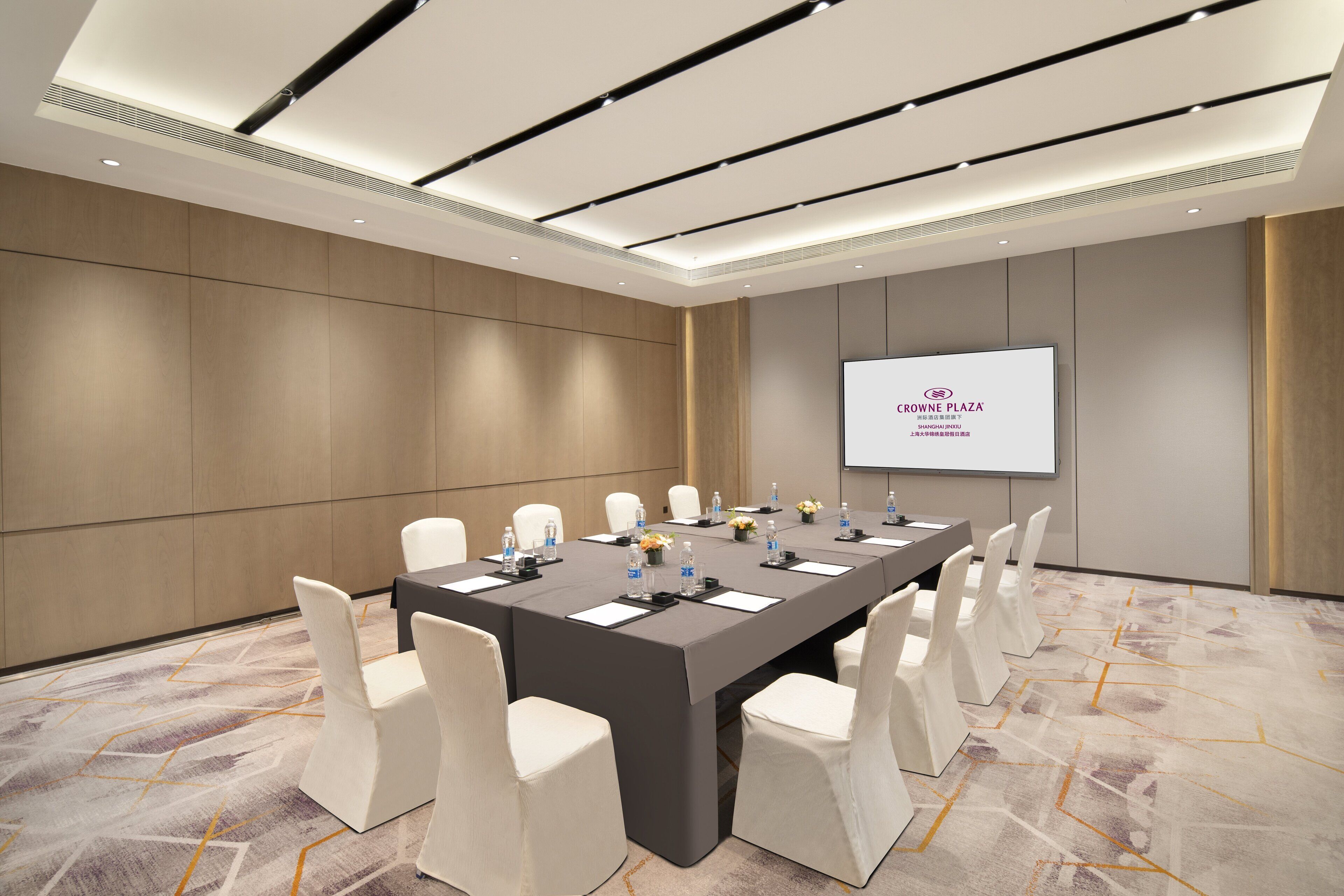 A conference room with a long table, white chairs, and a screen displaying "CROWN PLAZA".