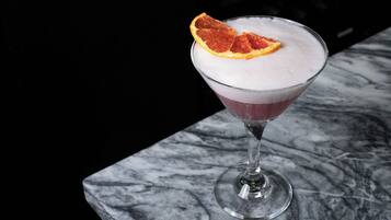 Un verre à martini contenant une boisson mousseuse et décoré d’une tranche d’orange séchée, le tout posé sur une surface en marbre.