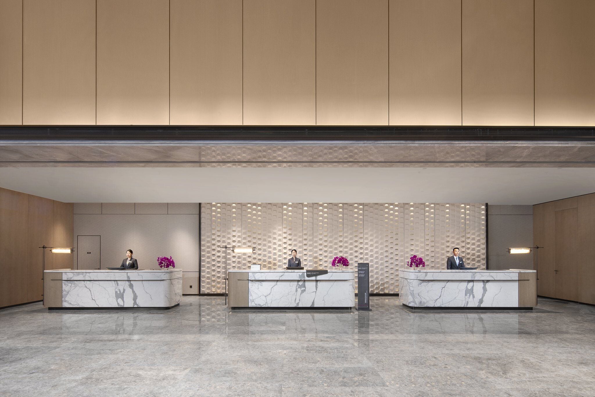 A reception area with marble counters, two receptionists, and a decorative wall with vertical panels.