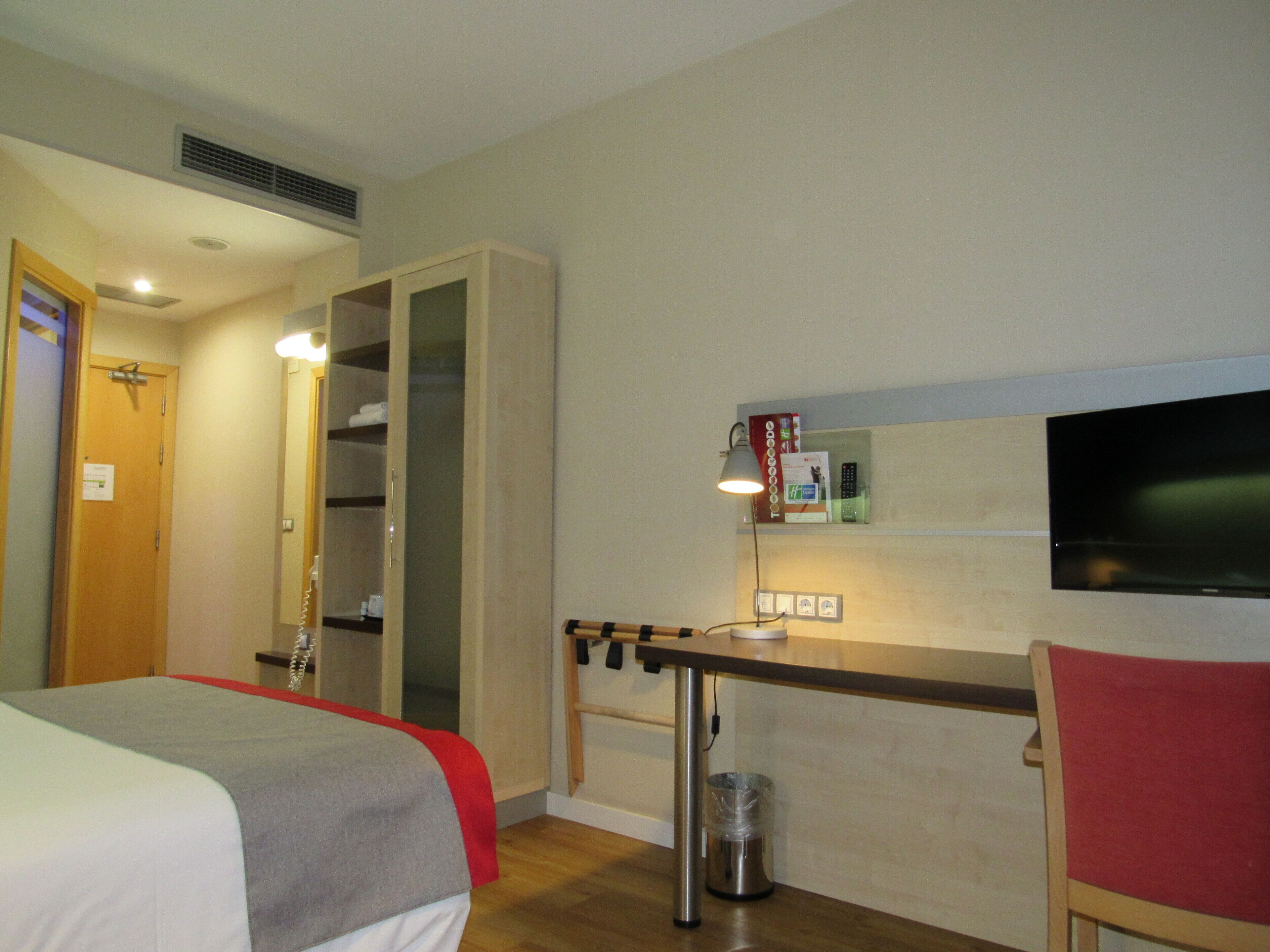 A hotel room with a bed, a desk, a chair, a TV, and a wardrobe.
