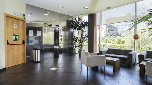 Un vestíbulo moderno con mostrador de recepción, ascensores y zona de estar con vistas al exterior.