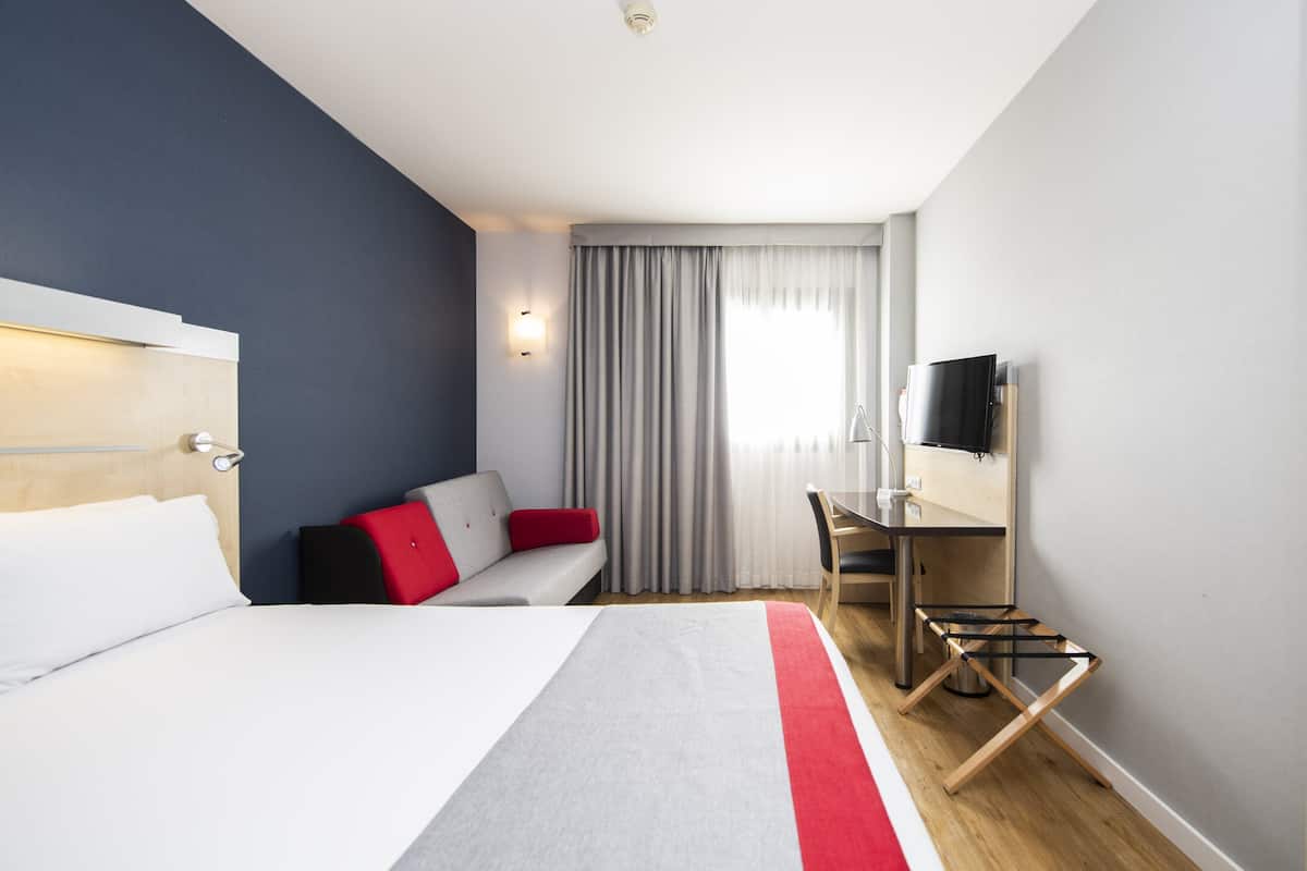 A hotel room with a bed, a desk, a television, and a window with curtains.