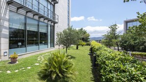 Un edificio moderno con amplios ventanales de vidrio, un césped cuidado y diversas plantas.