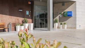 Entrada moderna de un edificio con un letrero de Holiday Inn Express, un banco y plantas en macetas.