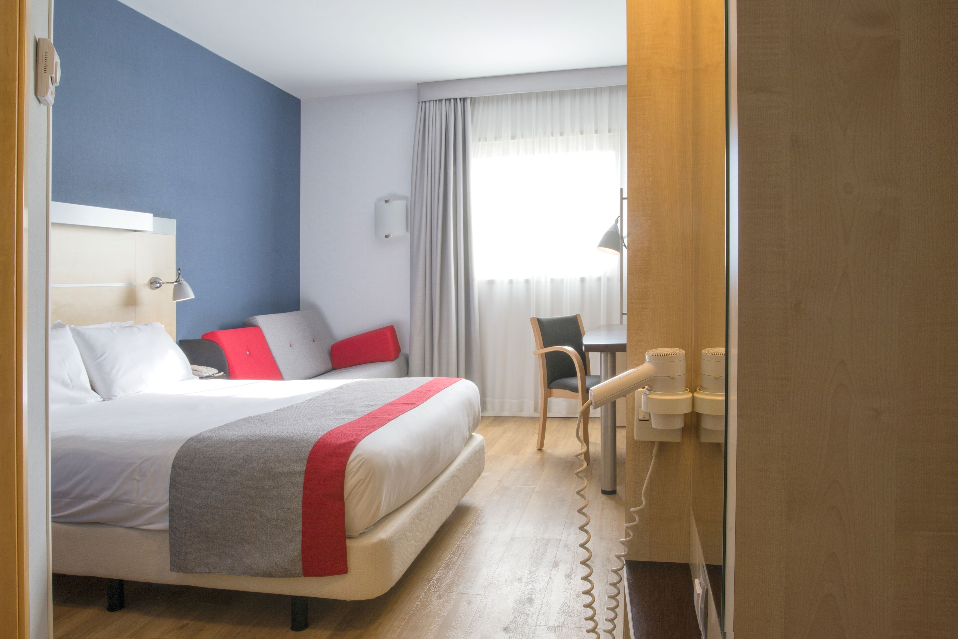 A hotel room with a bed, a desk, a chair, and a window with curtains.