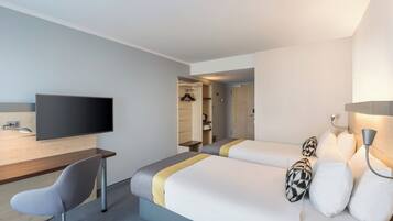 A hotel room with two beds, a desk with a chair, a flat-screen TV, and a lamp.