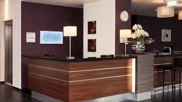 A hotel reception area with a wooden reception desk, a clock, and a vase with flowers.