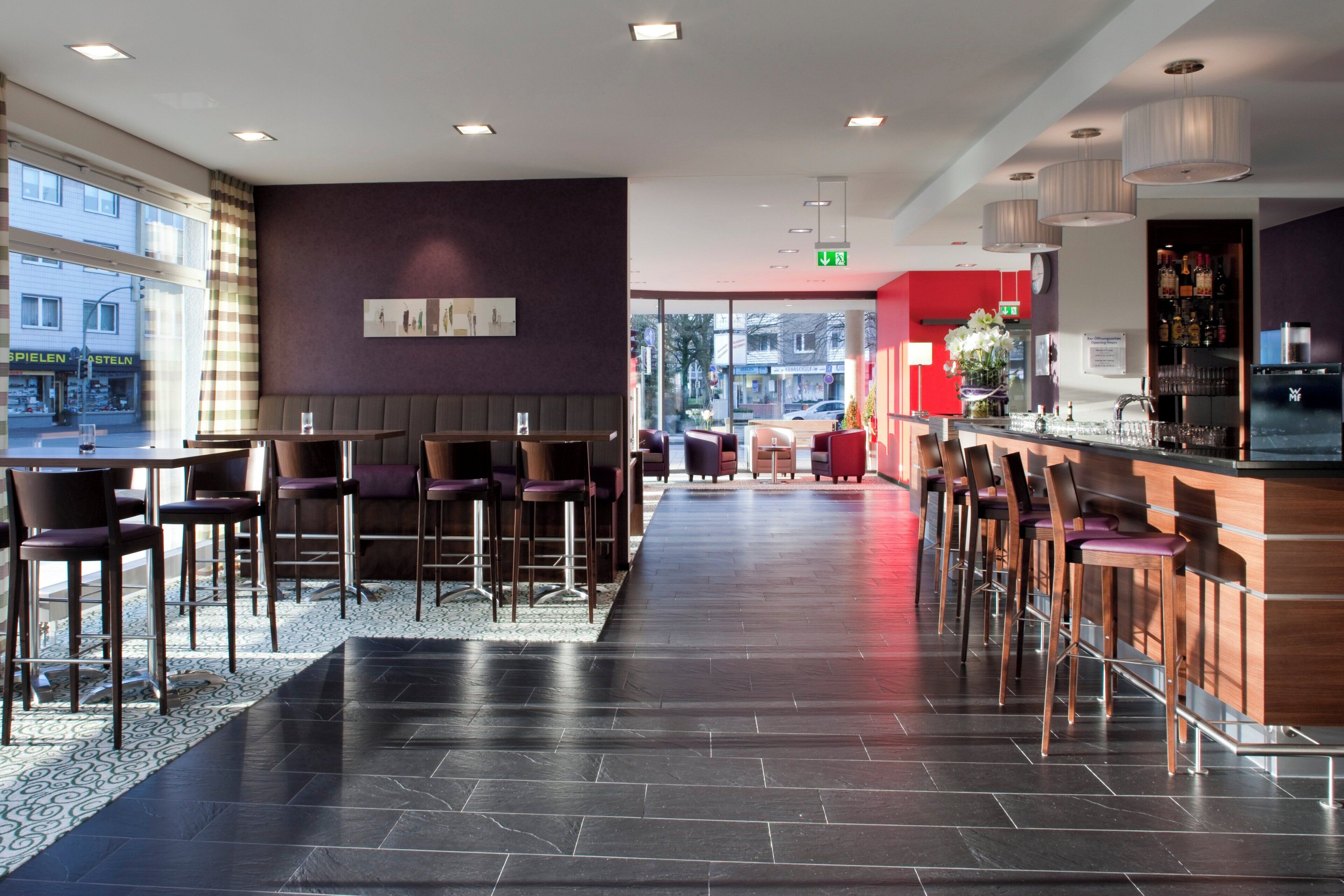 Eine moderne Bar mit hohen Hocker und einer Theke, ein Sitzbereich mit Tischen und Stühlen, und ein Boden mit Muster.