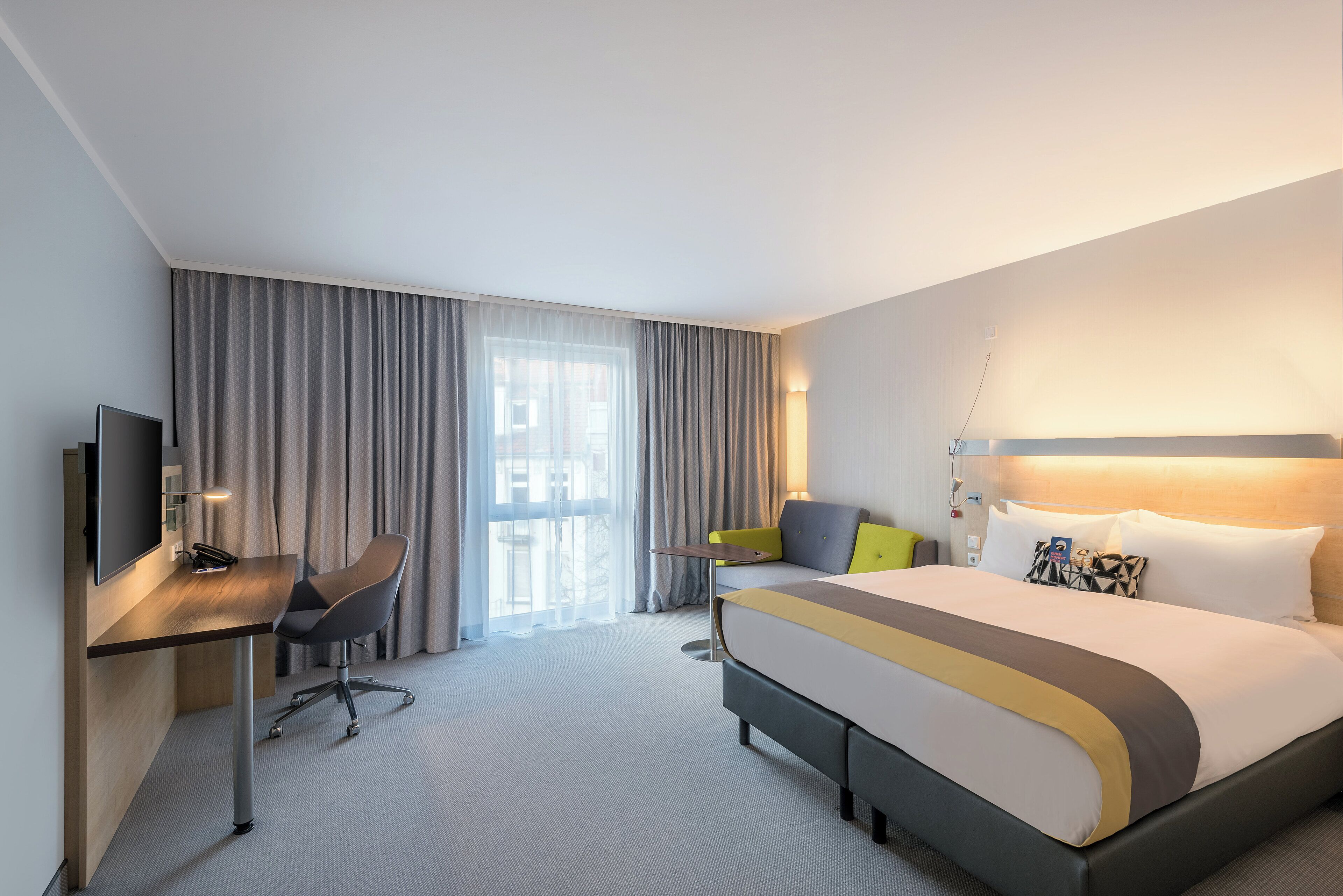 Een hotelkamer met een bed, een bureau, een stoel, een televisie en een raam met gordijnen.