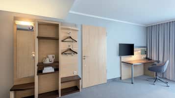 Ein Hotelzimmer mit einem Holfischschrank, einem Schreibtisch mit Stuhl, einem Flachbildfernseher und einem Bett.