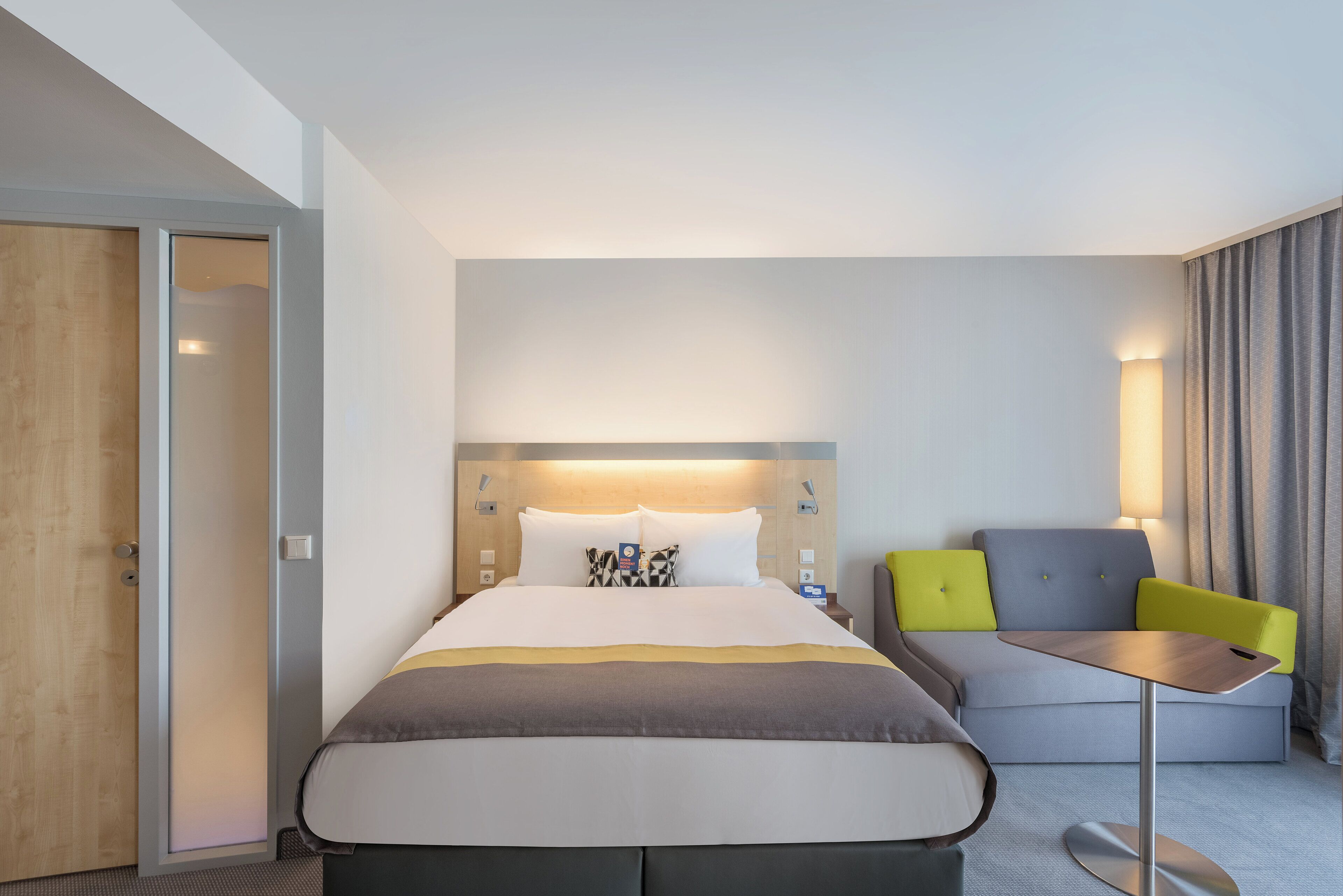 A hotel room with a bed, a desk, a chair, and a door.