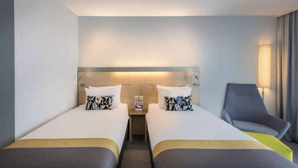 A hotel room with two beds, a nightstand, a chair, and a lamp.