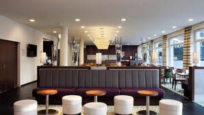 A modern hotel lobby with a central seating area, multiple tables, and a patterned carpet. - Holiday Inn Express Guetersloh by IHG (Guetersloh)