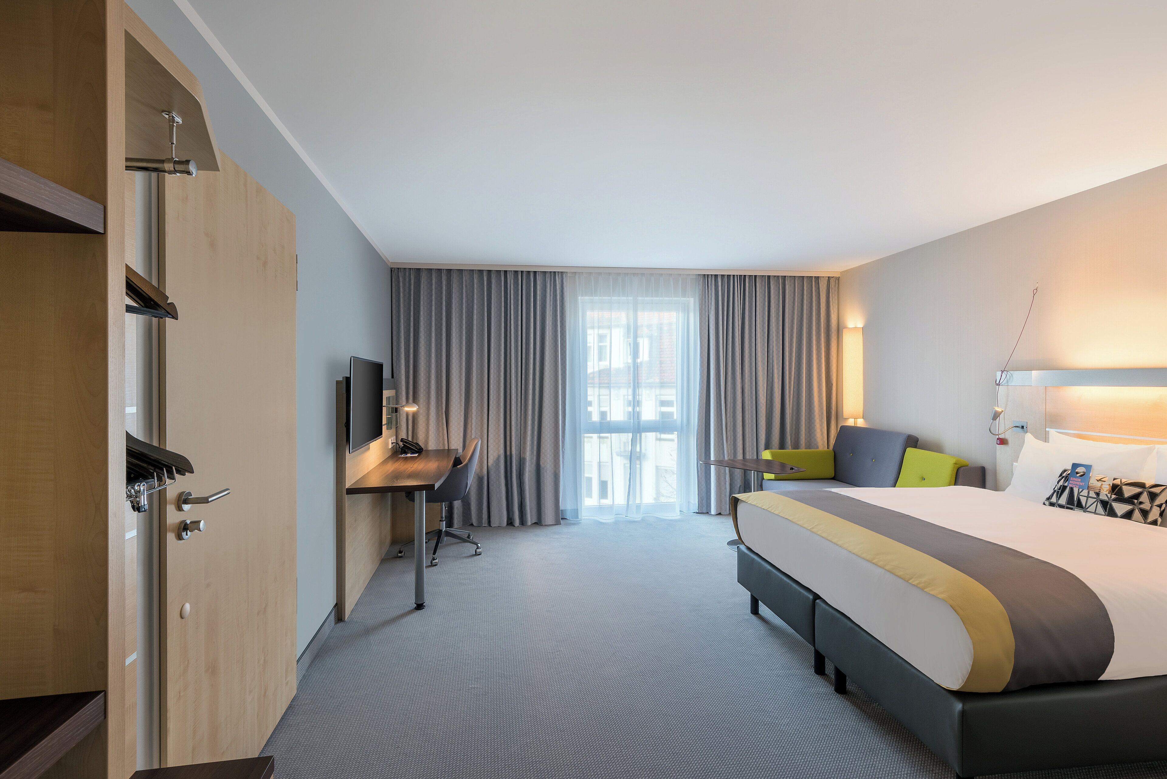 Une chambre d’hôtel équipée d’un lit, d’un bureau, d’une chaise, d’une télévision et d’une fenêtre avec des rideaux.
