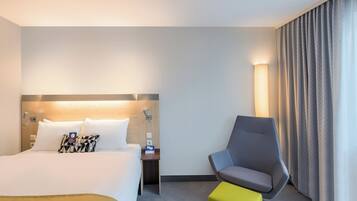 A hotel room with a bed, a chair, a nightstand, and a lamp.