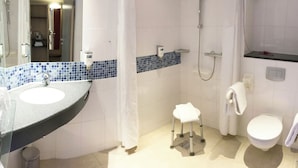 A bathroom with a sink, toilet, shower, and a small stool.