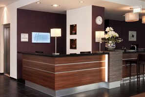 A modern reception desk with a clock, a digital display, and a vase with flowers. - Holiday Inn Express Guetersloh by IHG (Guetersloh)