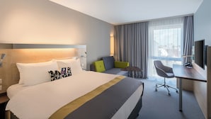 A hotel room with a large bed, a desk, a chair, and a TV.