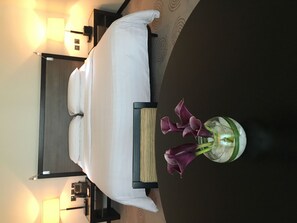 Habitación de hotel con cama, mesita de noche, lámpara y un jarrón con flores.