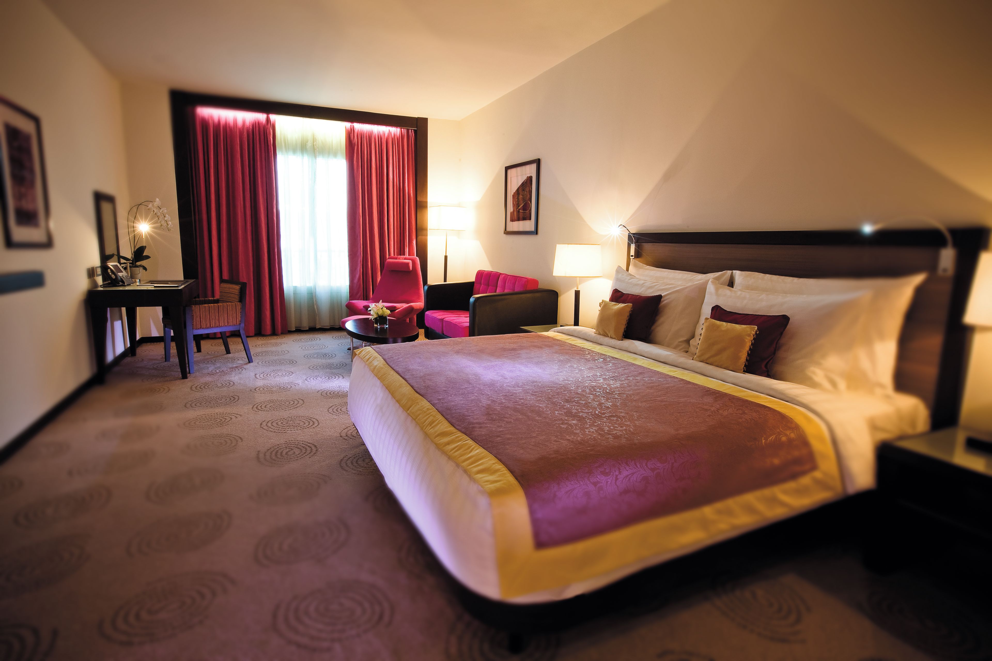 A hotel room with a large bed, a desk, a chair, and a window with curtains.