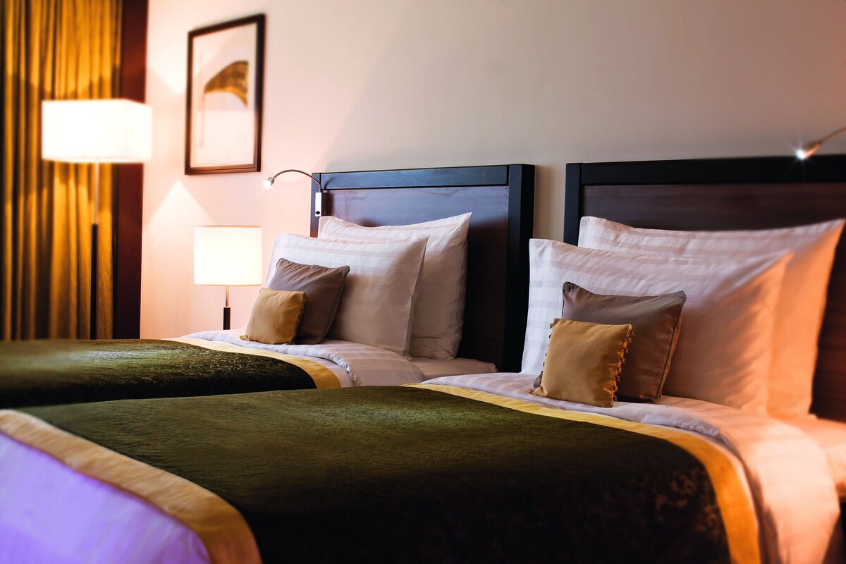 Une chambre d’hôtel avec deux lits, chacun doté d’une tête de lit, d’une table de chevet et d’une lampe.