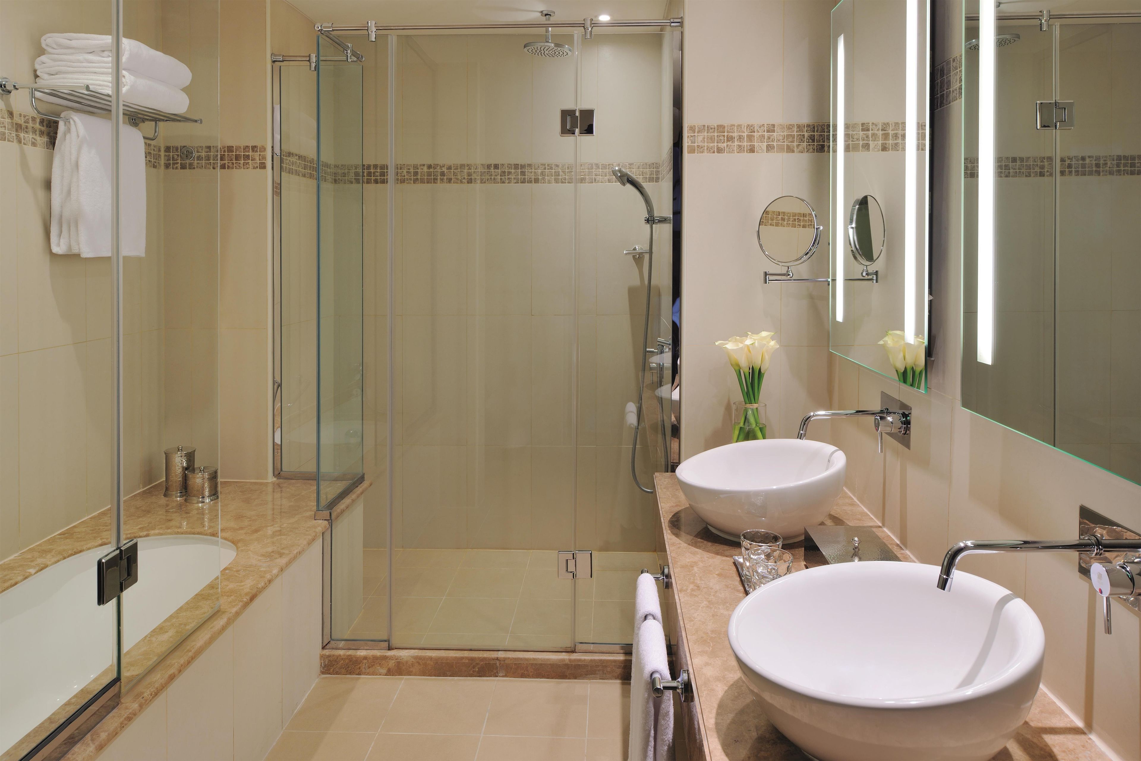 Ein modernes Badezimmer mit einer gläsernen Duschkabine, zwei Waschbecken und einem großen Spiegel.