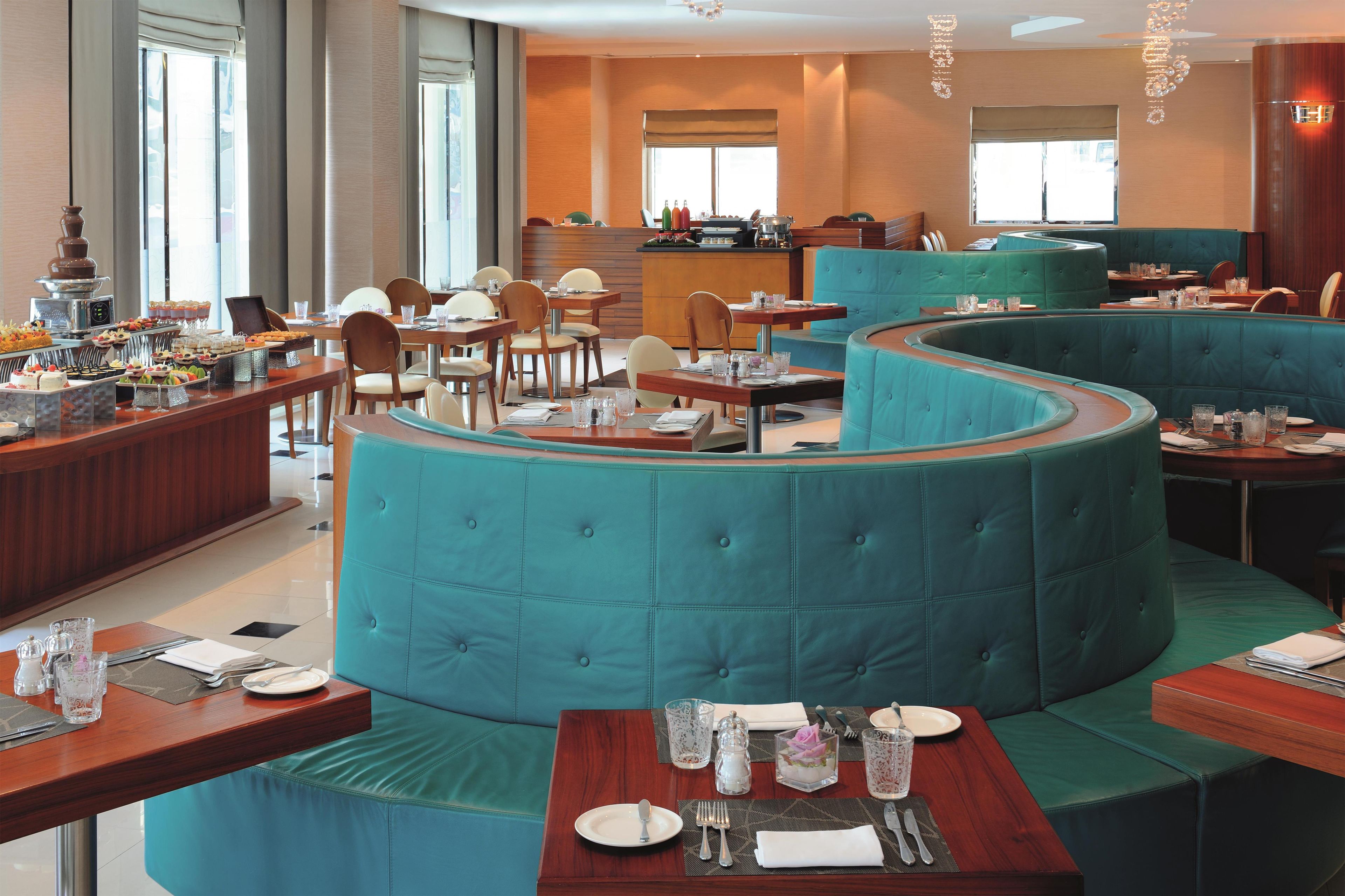 A restaurant with a curved seating area, multiple dining tables, and a buffet with various food items.
