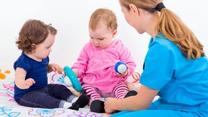A child in a pink outfit and another in a blue outfit sitting on a colorful mat with a woman in blue attire. - Avani Deira Dubai Hotel (Dubai)